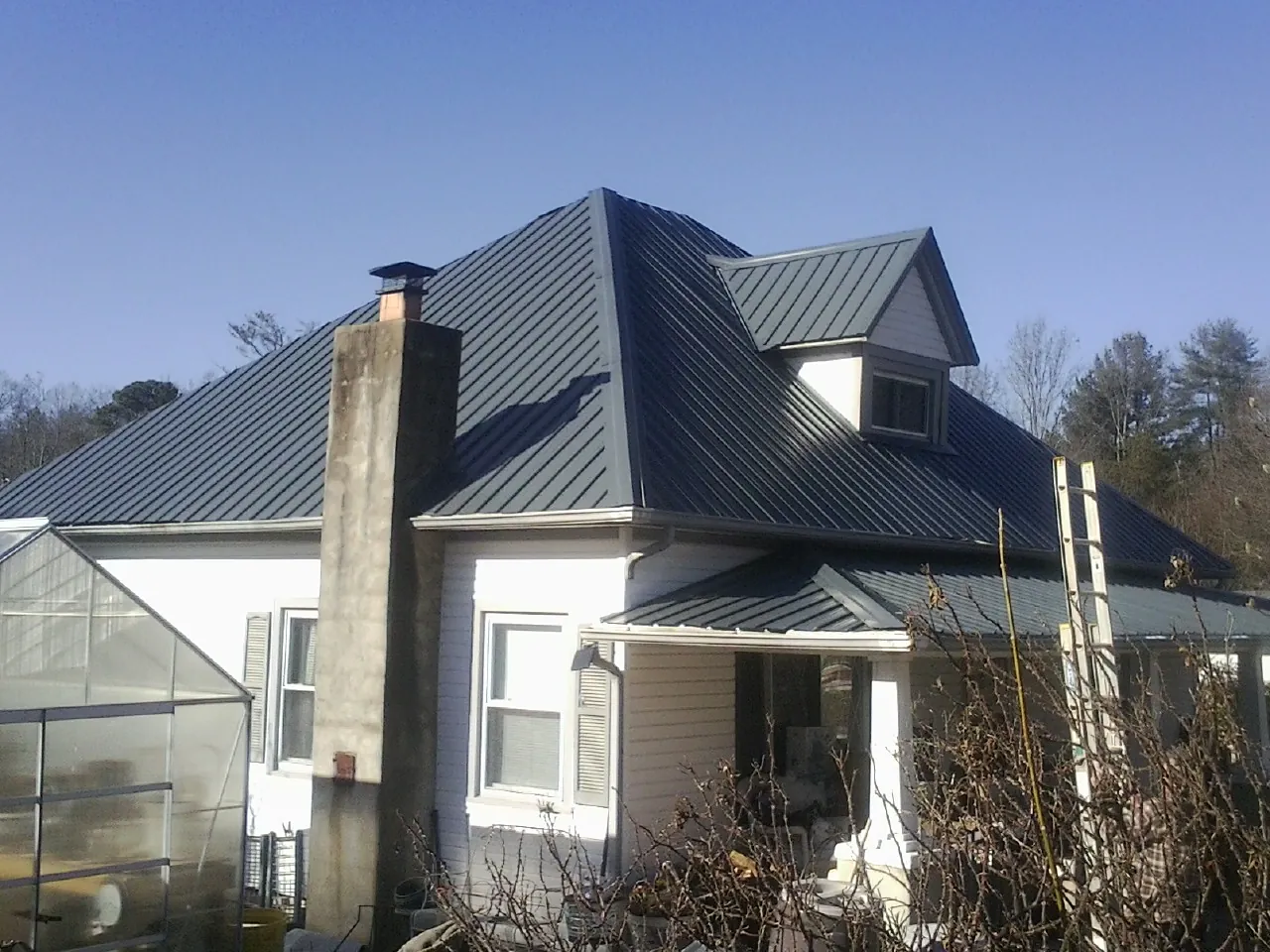 Dark blue standing seam metal roof on a white farmhouse with dormer — Slate & Tile Roof Repair by Roofing Brothers in Laredo