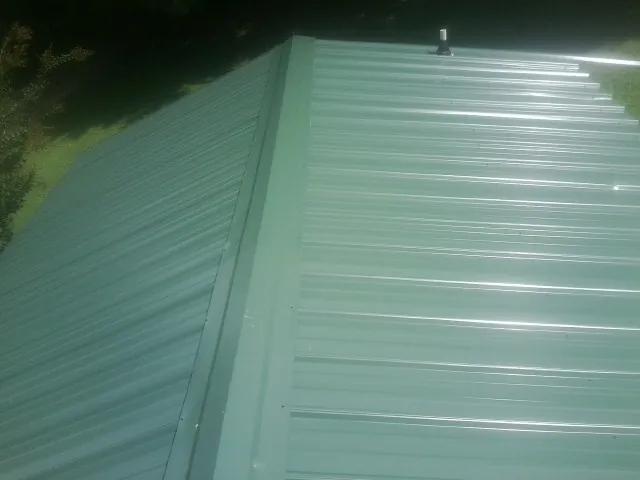 New green metal panels meeting at the ridge of a roof — Flat Roof Repair work by our crew in Laredo