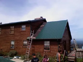 Green metal roof going on a two story log home with ladders set in Laredo